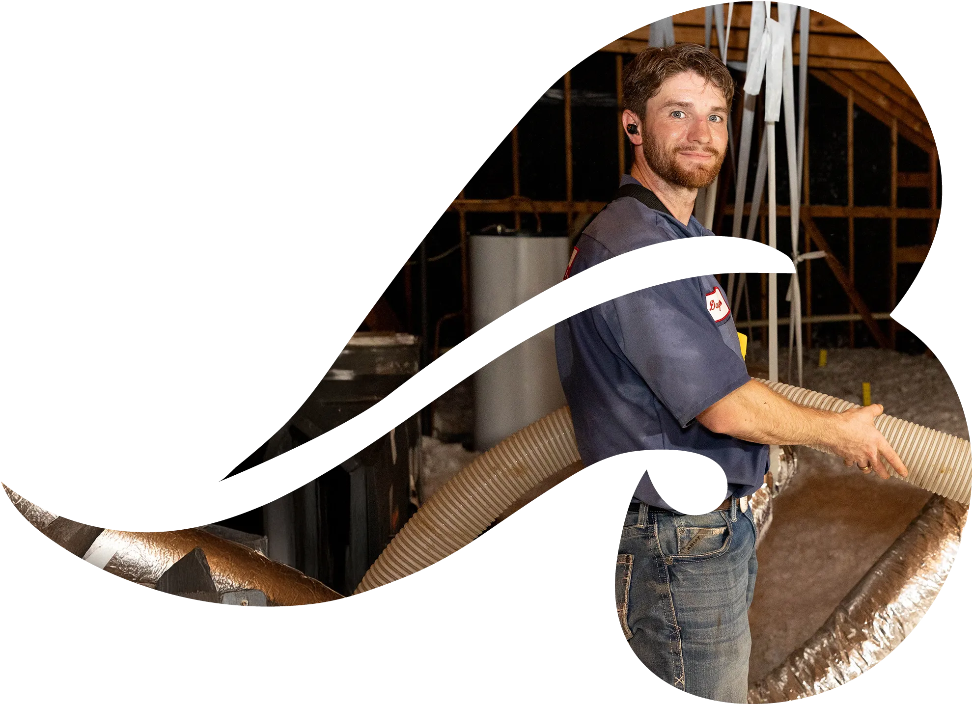 A man HVAC technician installing flexible duct insulation in an attic, smiling and holding a hose