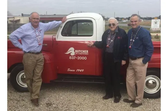 Three men standing beside a vintage red-and-white Butcher Air Conditioning pickup truck marked 'Since 1949'.