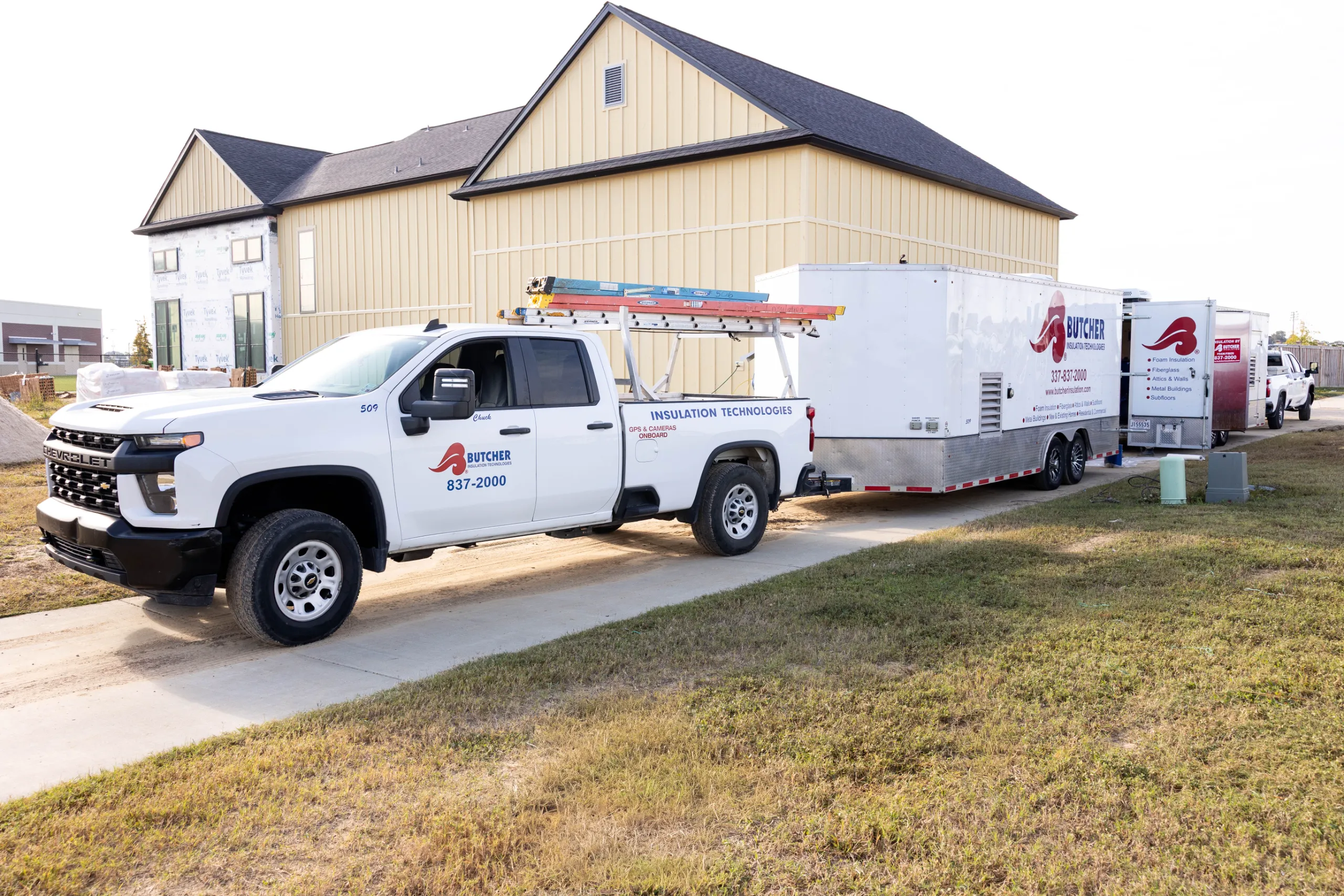 White Butcher Insulation pickup and trailer parked beside a beige house under construction