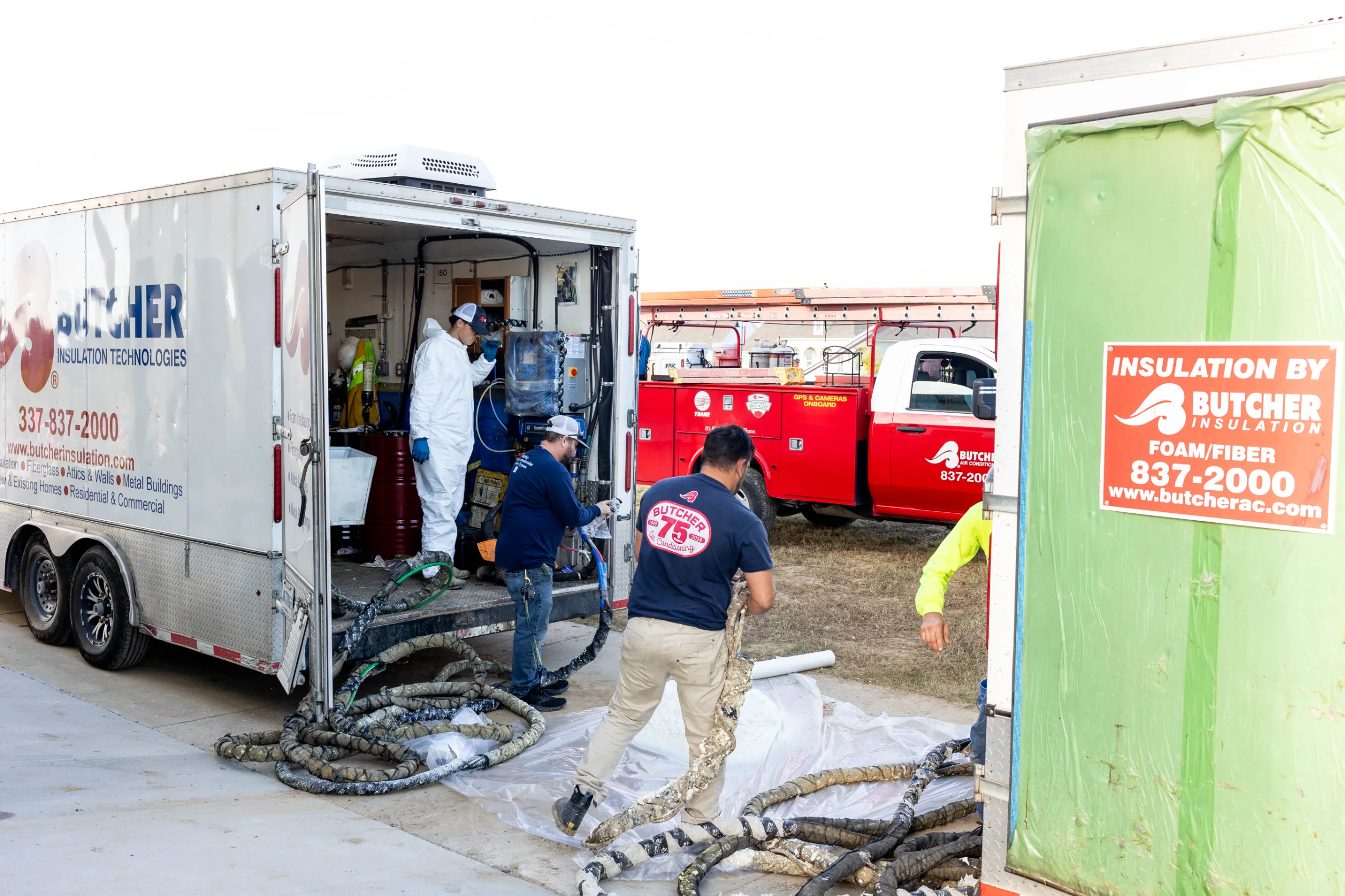 Butcher Insulation crew unloading hoses from a trailer, preparing spray foam insulation at a job site