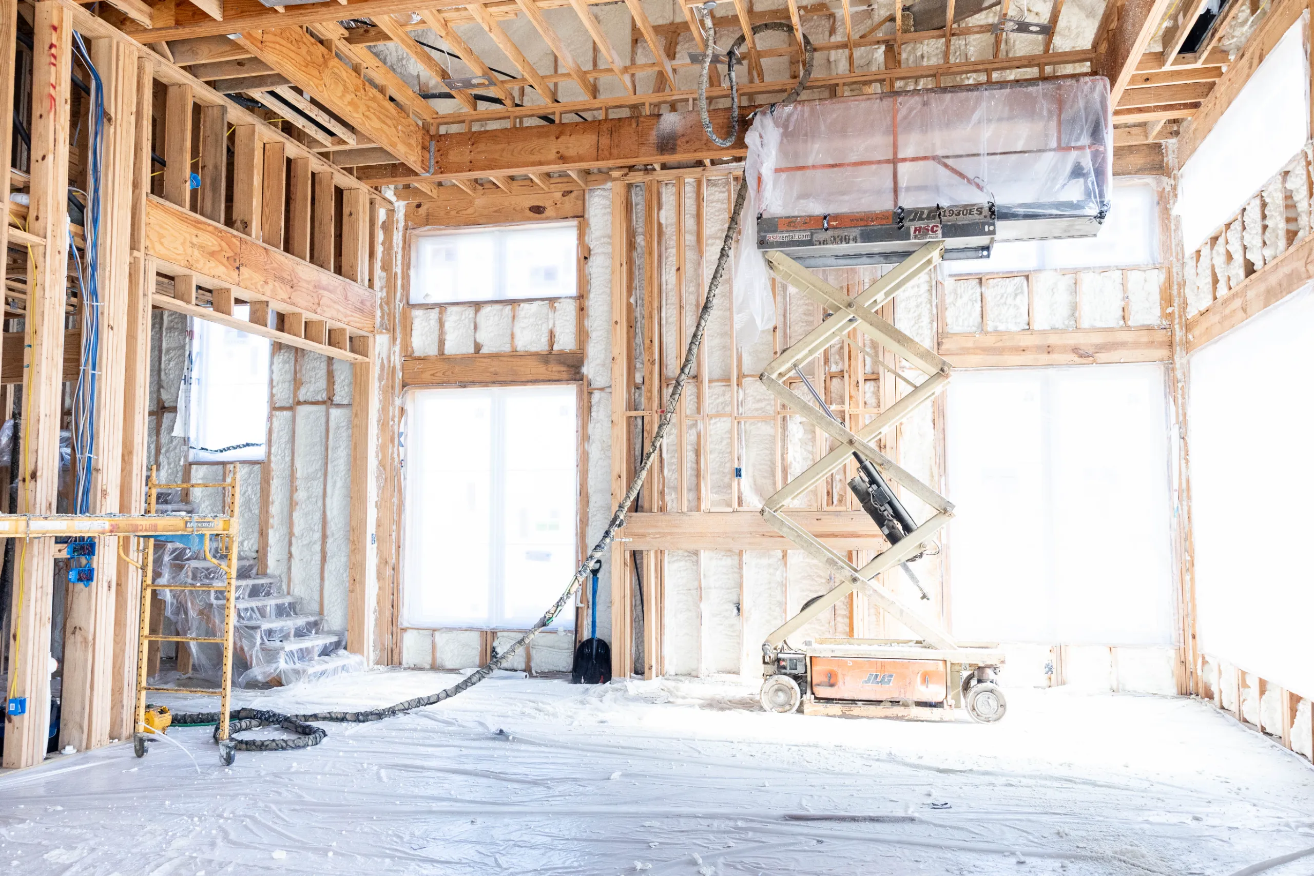 Interior residential construction with exposed wood framing, spray foam insulation, scaffolding and scissor lift equipment.