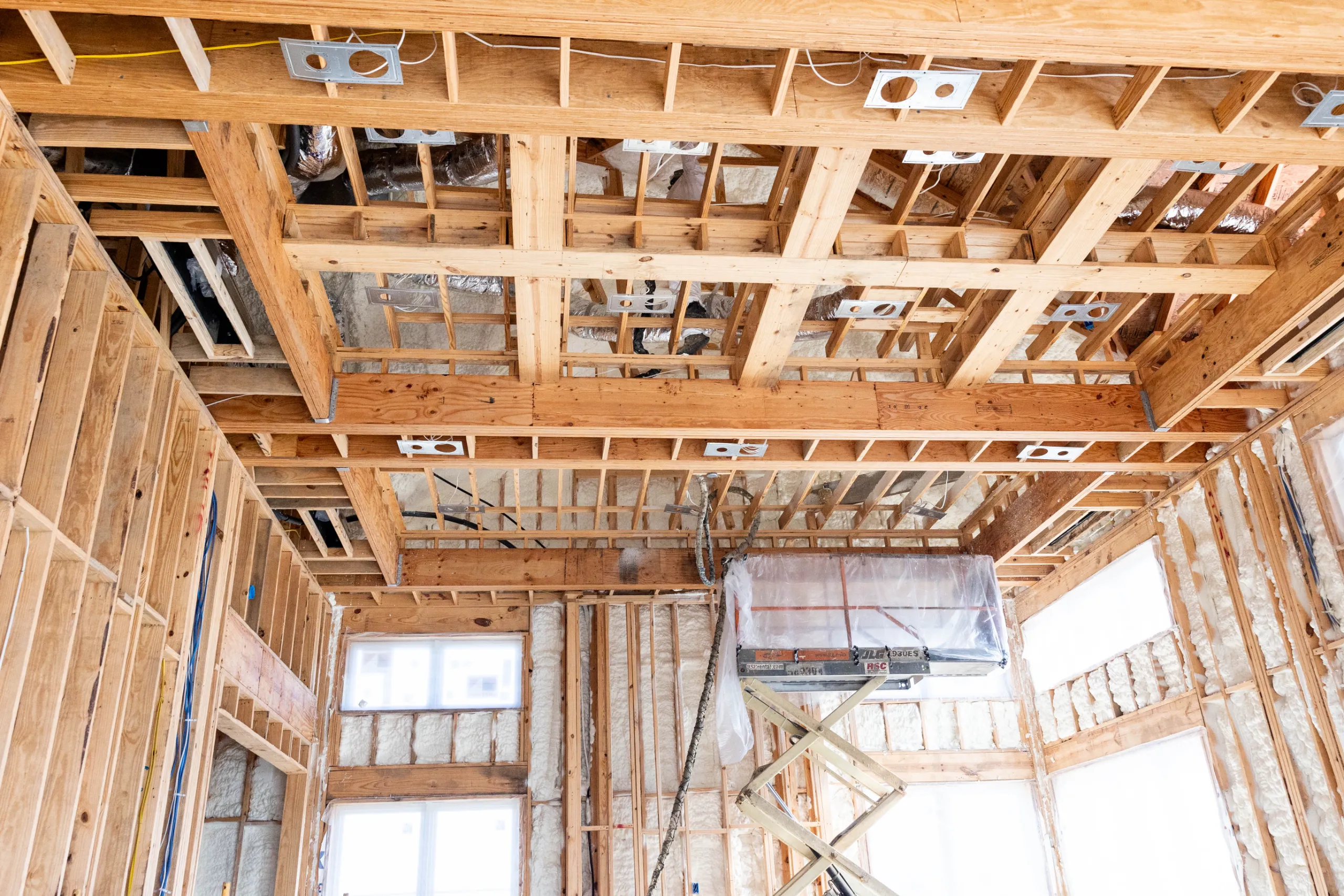 Exposed wooden ceiling joists and wall studs in home under construction with insulation, wiring, and recessed light boxes