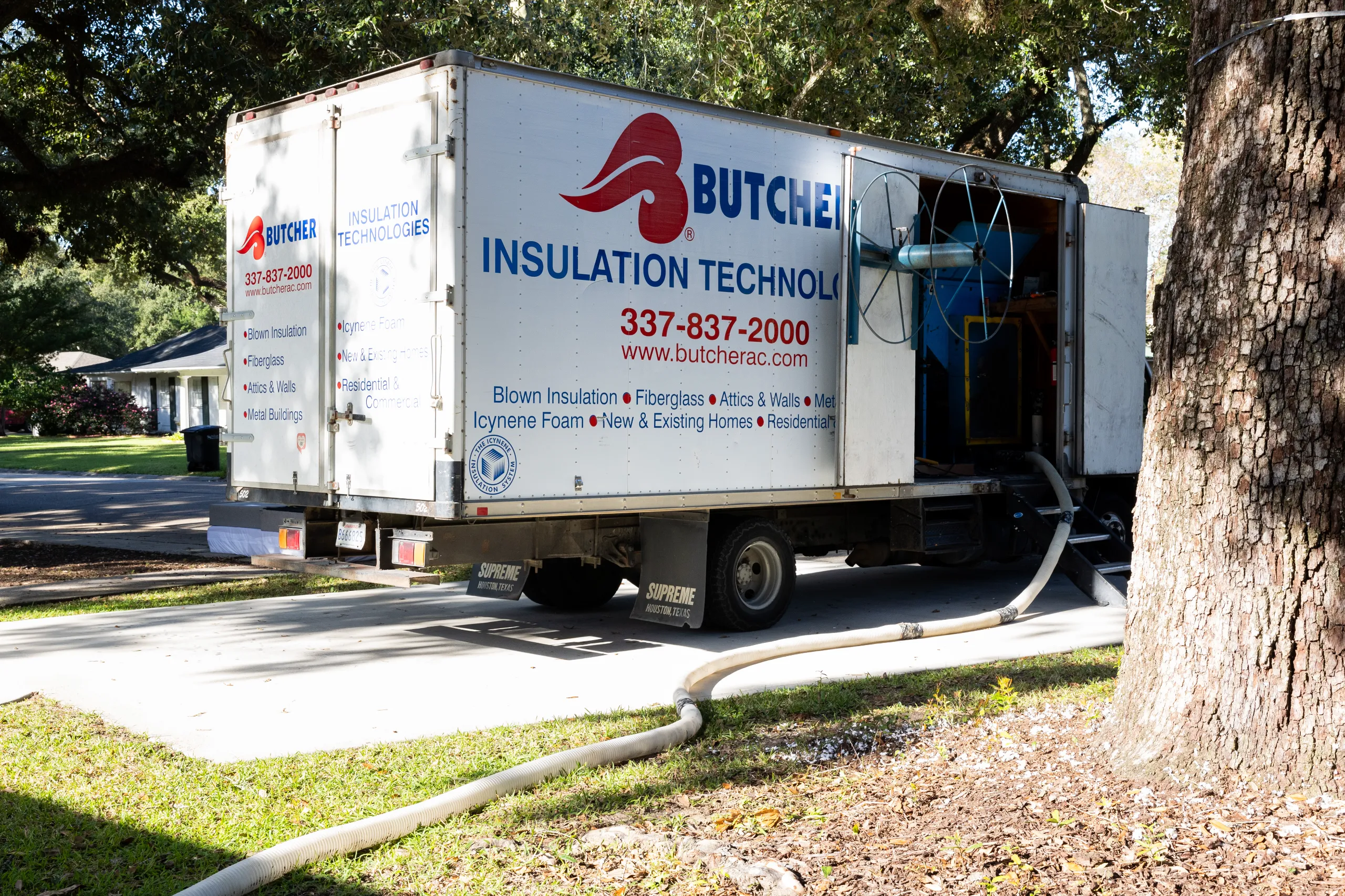 Butcher Insulation truck parked in a residential driveway with hoses running into a house for insulation.
