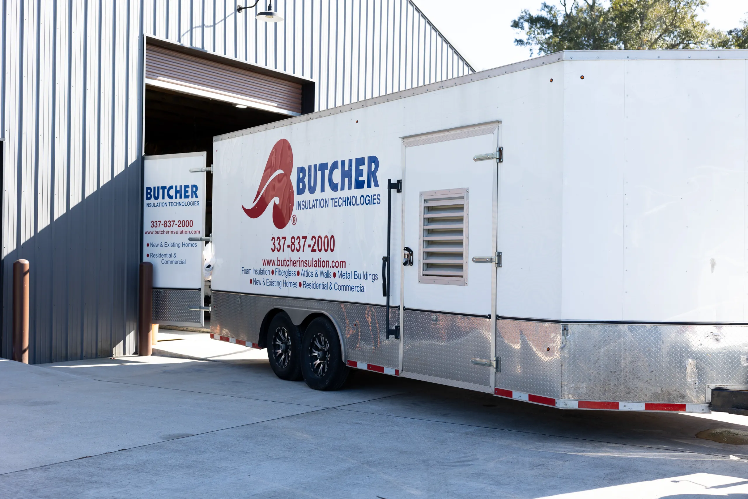 White Butcher Insulation trailer parked beside a corrugated metal warehouse with open bay and visible logo