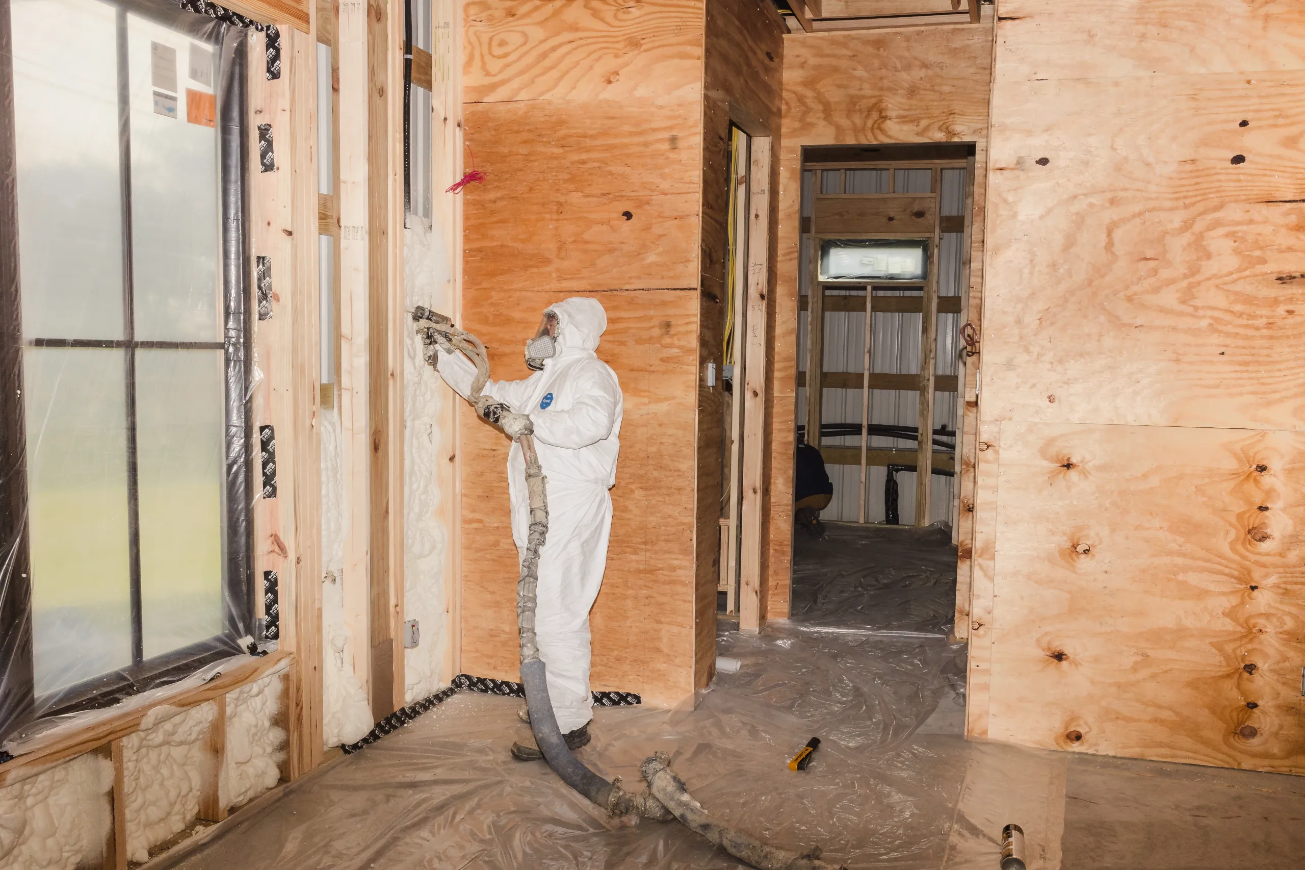 Worker in protective suit spraying spray foam insulation into wood stud walls during home construction