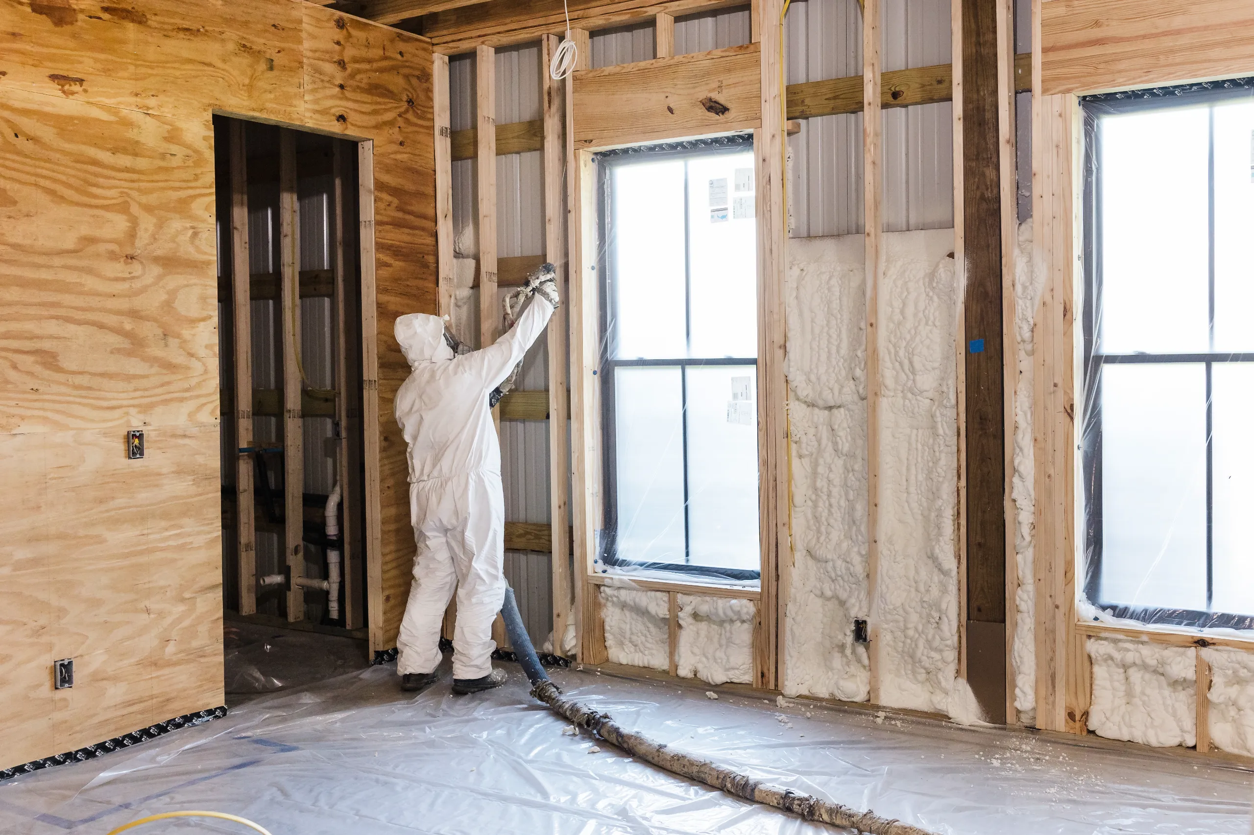 A worker in protective suit spraying spray-foam insulation into framed wood wall of a house under construction
