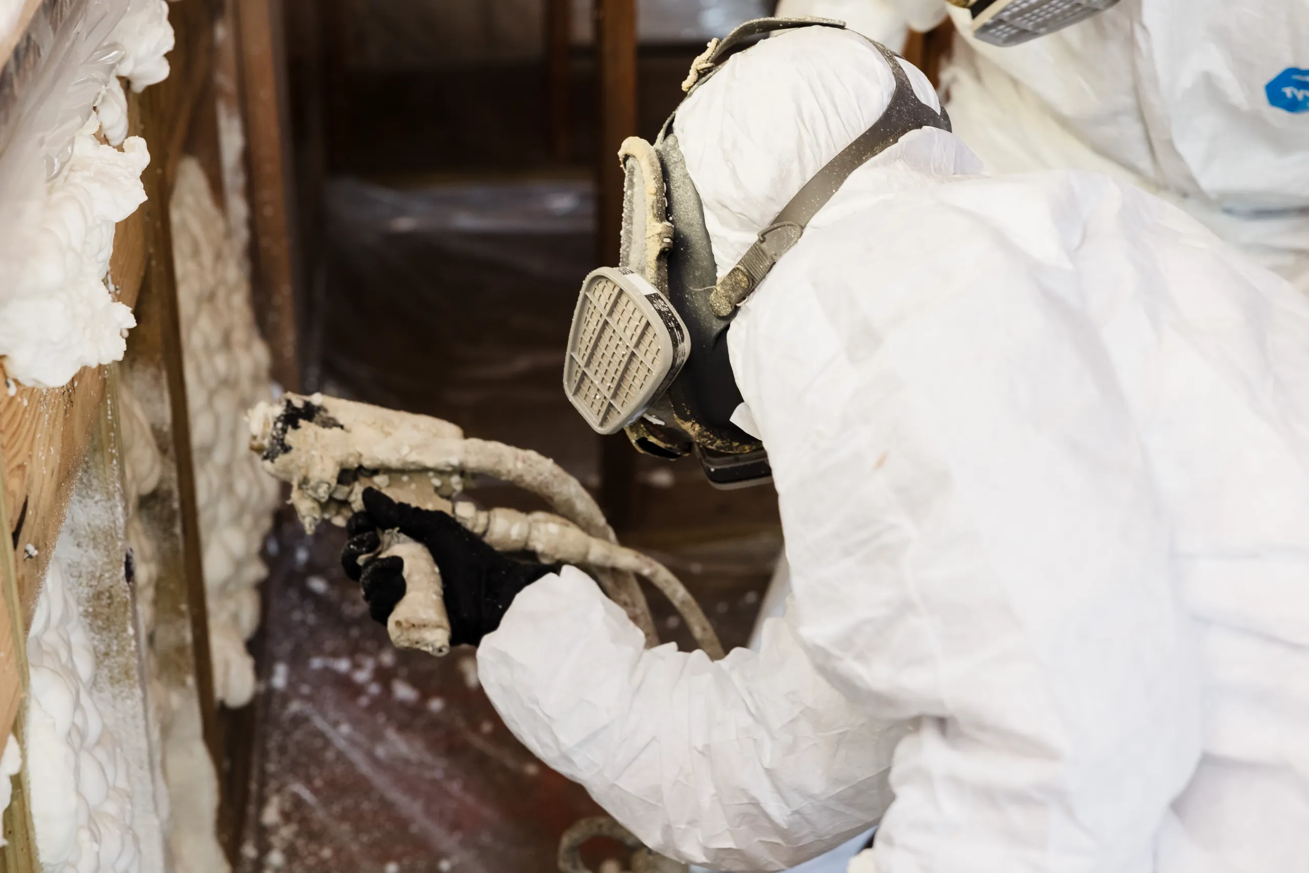 A person in protective suit and respirator installing spray-foam insulation in a wall cavity