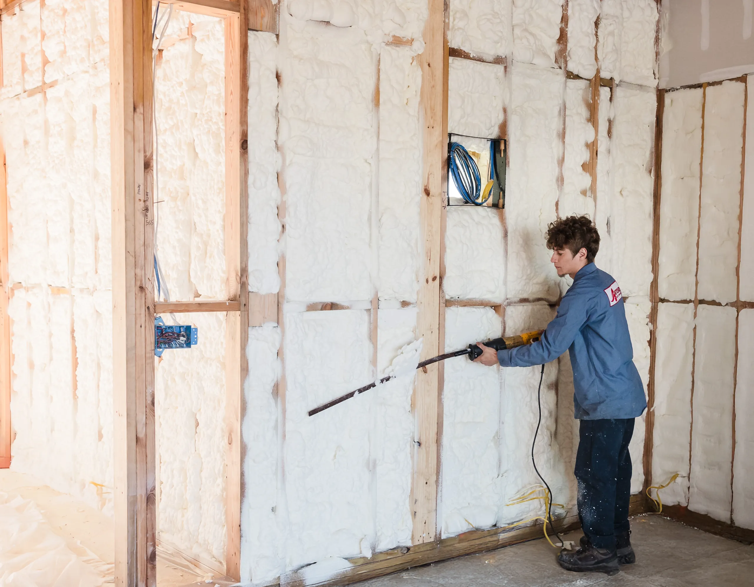 A man installing spray foam insulation in a wood-stud interior wall during residential construction