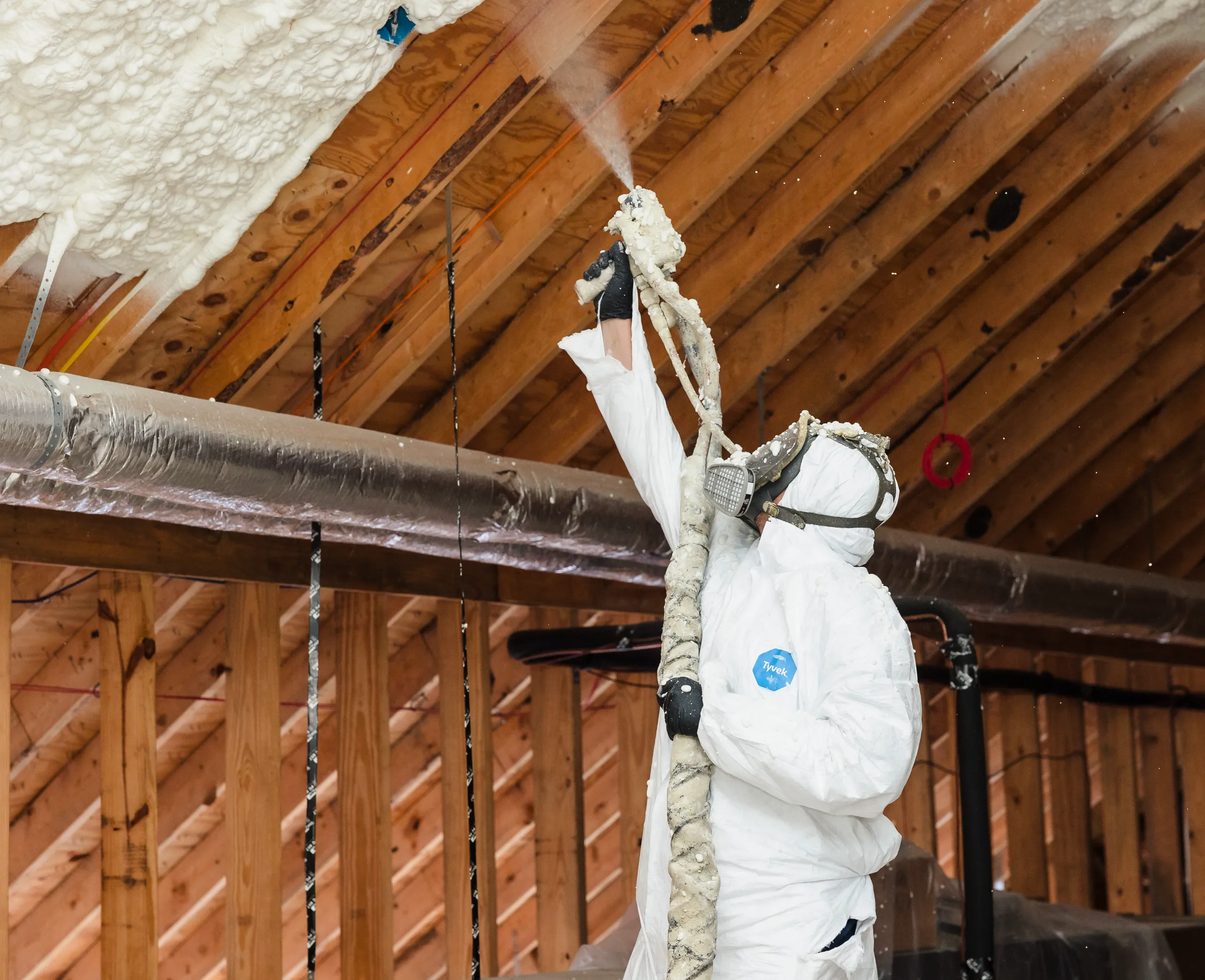 A worker in protective suit and respirator spraying spray-foam insulation onto attic rafters