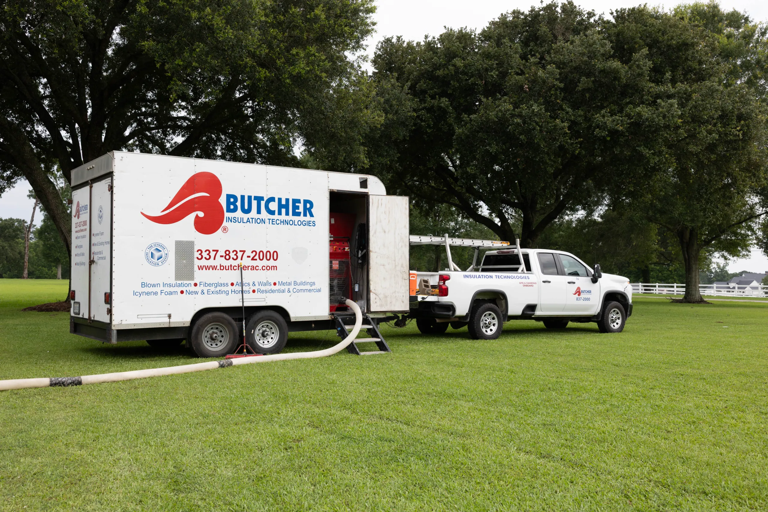 White Butcher Insulation Technologies truck and trailer parked on grass beneath large trees, hoses connected for insulation