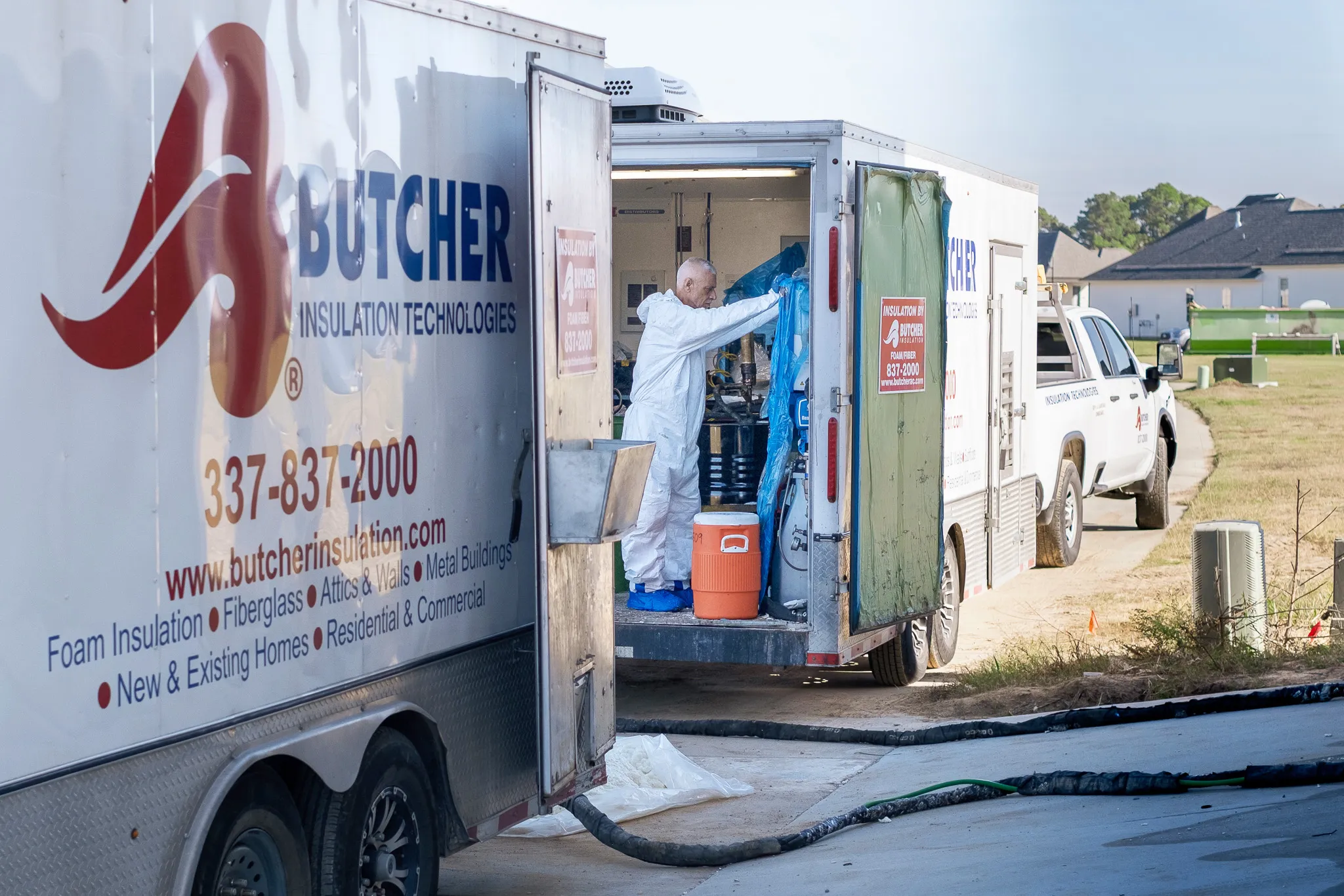 Worker in white protective suit handling insulation equipment from Butcher Insulation truck at a home.