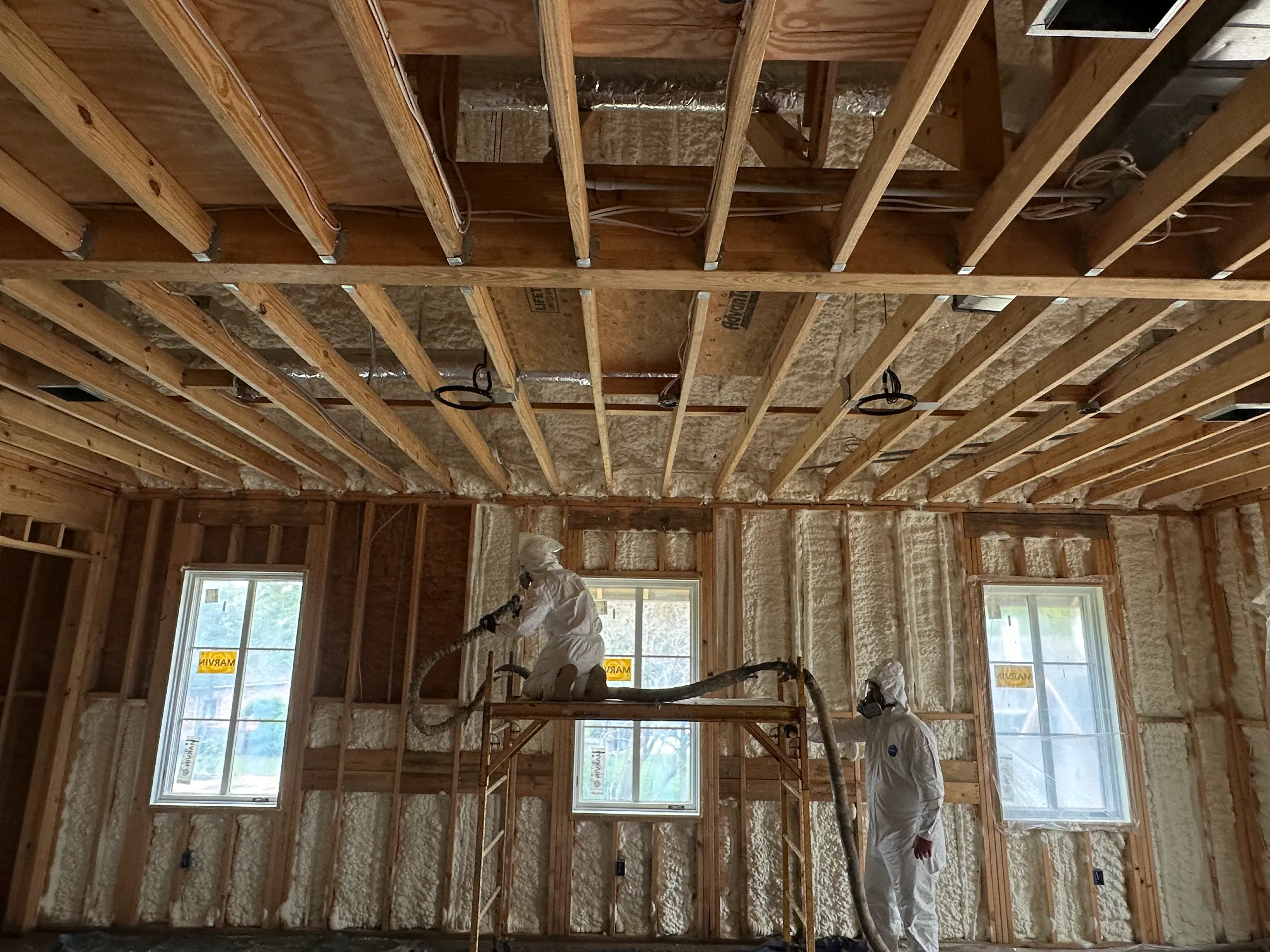 Workers in protective suits spraying spray-foam insulation into framed home's ceiling and walls