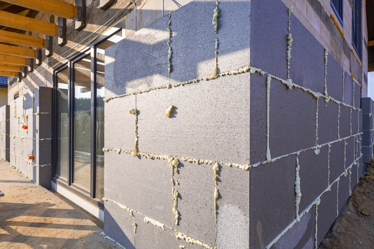 Exterior of house under construction with gray insulation blocks and expanding spray-foam sealant at panel joints.
