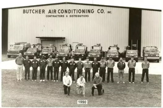 1990 Butcher Air Conditioning Co. team standing with fleet of service trucks in front of company building